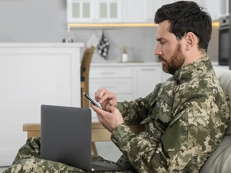 Military personnel using laptop and phone on couch